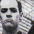 Pixelated static image of a person with dark hair and a white shirt against a light background with scattered dark shapes.