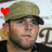 Pixelated image of a person wearing a green military-style cap with a red heart symbol on the left side, dark sunglasses, and a dark jacket against a light background.