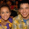 Two people smile at the camera in a crowded indoor setting with blurred background figures.