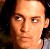 Pixelated close-up of a person's face with light skin tone, dark hair, and neutral expression against dark background.