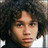 Pixelated close-up of a person with dark curly hair and light skin, wearing a white shirt against a blurred background.