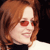 Pixelated close-up of a person with light brown hair wearing red-tinted sunglasses and a white top against a dark background.
