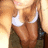 Pixelated image of a person wearing a white tank top and dark jacket, with light brown hair and a blurred background.