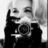Black-and-white pixelated image of a person holding a camera with both hands, positioned to take a photograph.