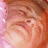 A pixelated close-up of a person's face with light brown hair, pink background, and subtle facial features.