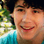 A person with dark curly hair wearing a light blue shirt smiles in a of six identical frames with green foliage background