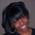 Pixelated close-up of a person with short dark hair, smiling broadly showing teeth, wearing large hoop earrings against a gray background.