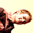 Pixelated static image of a person's face and upper body in profile view with brown hair, visible ear, and dark clothing against a light background.