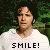 Pixelated image of a person in a white shirt with 'SMILE!' text below, set against a dark green background.