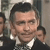 Static pixelated image of a person in a dark suit with a white shirt and patterned tie, partially cropped on the left and right edges.
