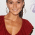 A static pixelated image of a person wearing a deep red V-neck top with visible shoulder straps, smiling against a light background.