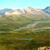 A pixelated landscape scene with layered green and brown terrain under a light blue sky with faint clouds.