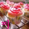 A static image of multiple cupcakes with pink and white frosting arranged on a metal rack, with a pink smiley face emoticon in the bottom left corner.