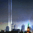 Pixelated cityscape with two vertical light beams and text reading "We will never forget" on a black background.