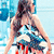 A woman with long dark hair in a blue and white patterned swimsuit stands facing away from the viewer, arms slightly outstretched against a light blue background.