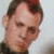 Pixelated close-up of a person's face with light skin tone, dark hair, and a neutral expression against a light background.