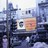 Pixelated static image showing a blurred urban scene with indistinct buildings and a central rectangular shape containing faint text.