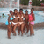Group of people in swimwear posing by a pool, with one person wearing red top and pink bottoms.