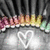 A pixelated image shows a blurred horizontal arrangement of colorful shapes resembling flowers or abstract forms against a dark background with light streaks.