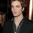 Static 48x48 pixel icon showing a close-up of a person with light skin and brown hair wearing a dark jacket over a white shirt, set against a blurred background with warm tones.