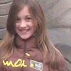 A person with long light brown hair wearing a dark top, holding a yellow neon sign and a small rectangular object with text.