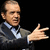 A pixelated image of a man in a suit gesturing with his right hand, with text reading "Wassa Mattah" and "Whichu!?" on a black and gray background.