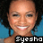 Pixelated close-up of a smiling person with dark curly hair against blue background, text 'Syesho' in white block letters on black bar at bottom.