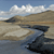 Pixelated landscape with blue sky, white clouds, brown hills, and dark water reflections.