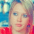 Pixelated close-up of a person with light hair wearing red clothing against a blue and green background.