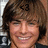 Pixelated close-up of a smiling person with brown hair and light skin, wearing a dark top against a blurred background.