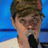 Pixelated close-up of a person with short brown hair wearing dark clothing against a blue background.