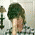 A person with dark curly hair wears a checkered shirt, holding a light-colored object near their face in a pixelated image.