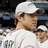 Pixelated image of a person wearing a white cap and white shirt with a red and blue emblem, set against a dark background with blue and gray elements.