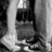 Black-and-white pixelated image of a figure in dark clothing holding an object, standing near vertical structures with light and shadow gradients.