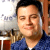 Static pixelated image of a person in blue clothing with blurred background elements including partial text and furniture.