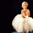 A blonde woman in a white dress sits with hands clasped, then stands and turns to the side as her skirt billows outward.