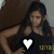 A pixelated image shows a person with long dark hair wearing a dark sleeveless top with a white heart symbol on the chest, seated against a brown background with a light gray area on the right.