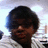 Pixelated portrait of a person with dark curly hair wearing a white shirt against light background.