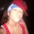 A person wearing a red cap with blue trim and red sleeveless top, smiling while touching their neck in three
