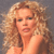 Pixelated close-up of a person with voluminous curly light brown hair against a solid gray background.