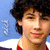 A person with curly dark hair wears a red and white collared shirt against a blue background with faint light patterns.