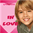 A static pixelated image shows a person with light brown hair and a green top on the right, next to a pink heart-shaped graphic containing red text reading 'IN LOVE' on the left.