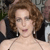 A pixelated close-up of a person with curly brown hair wearing a black strapless dress and a thin necklace, set against a blurred background.