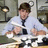 A pixelated image shows a person in a light blue shirt and dark tie seated at a table with white dishes, next to bold black text on pink background reading "where's my jim halpert?".
