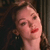 A static pixelated image shows a person with light skin, dark hair, and red lips, wearing a dark top with a small earring, against a dark background.