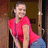 A pixelated image of a person wearing a bright pink short-sleeve top and light blue pants, standing indoors with a wooden door in the background.