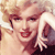 Pixelated close-up of a smiling person with light-colored hair, red lips, and a white glove on the right hand, set against a light background.