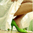 A pixelated image shows a person's lower body wearing green high-heeled shoes and brown pants, with one foot raised against a light background.
