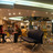 Pixelated static image of a theater interior with wooden flooring, dark seating, and a stage area under overhead lighting.
