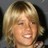 Static pixelated image of a person with light brown hair and closed eyes smiling, set against a dark background.